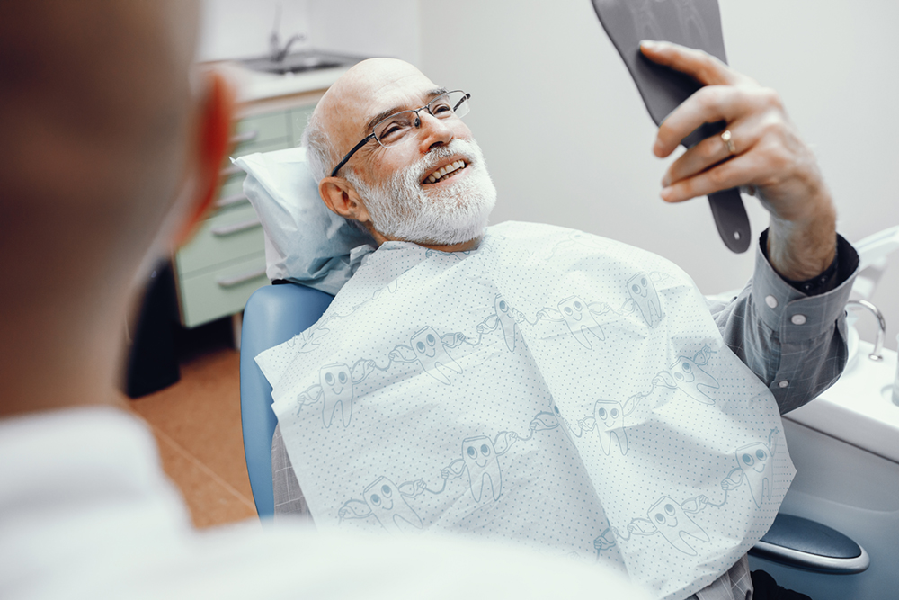 An older man looking at his teeth in a small mirror at the dentist, showing the results of periodontal surgery